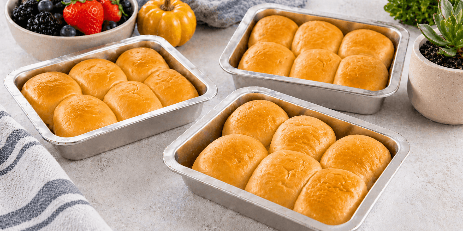 Pans of fresh-baked kolache rolls on a counter with bowls of berries and herbs